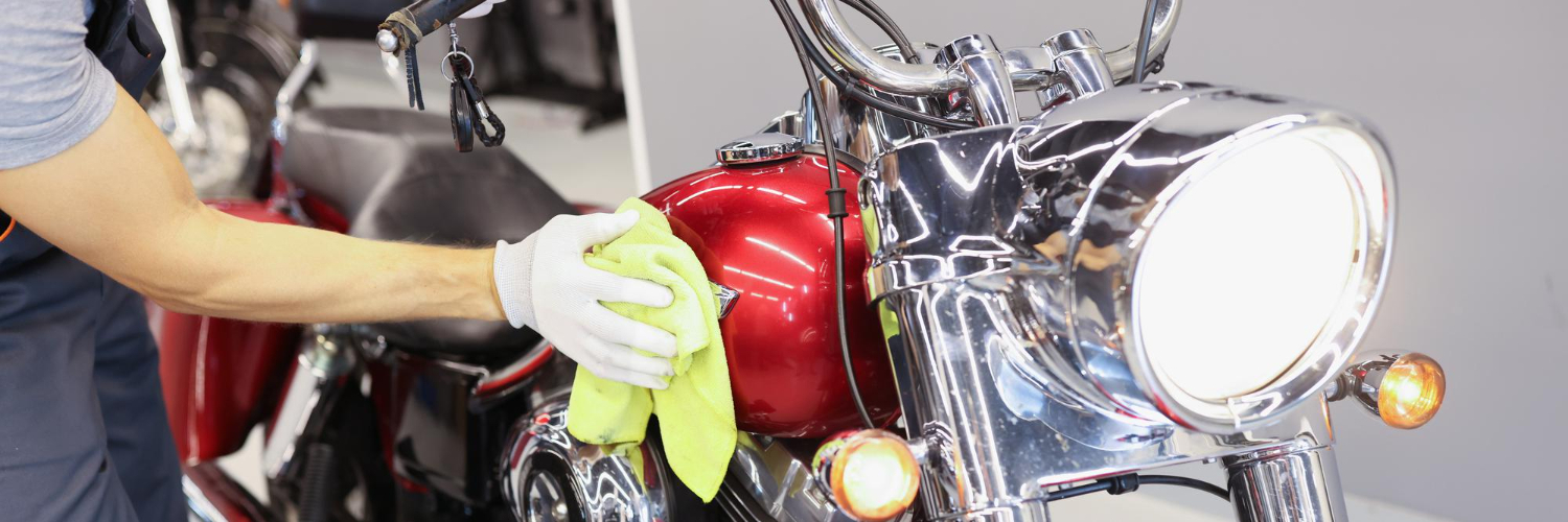 A man uses a microfiber cloth to polish the metal take of a motorcycle.