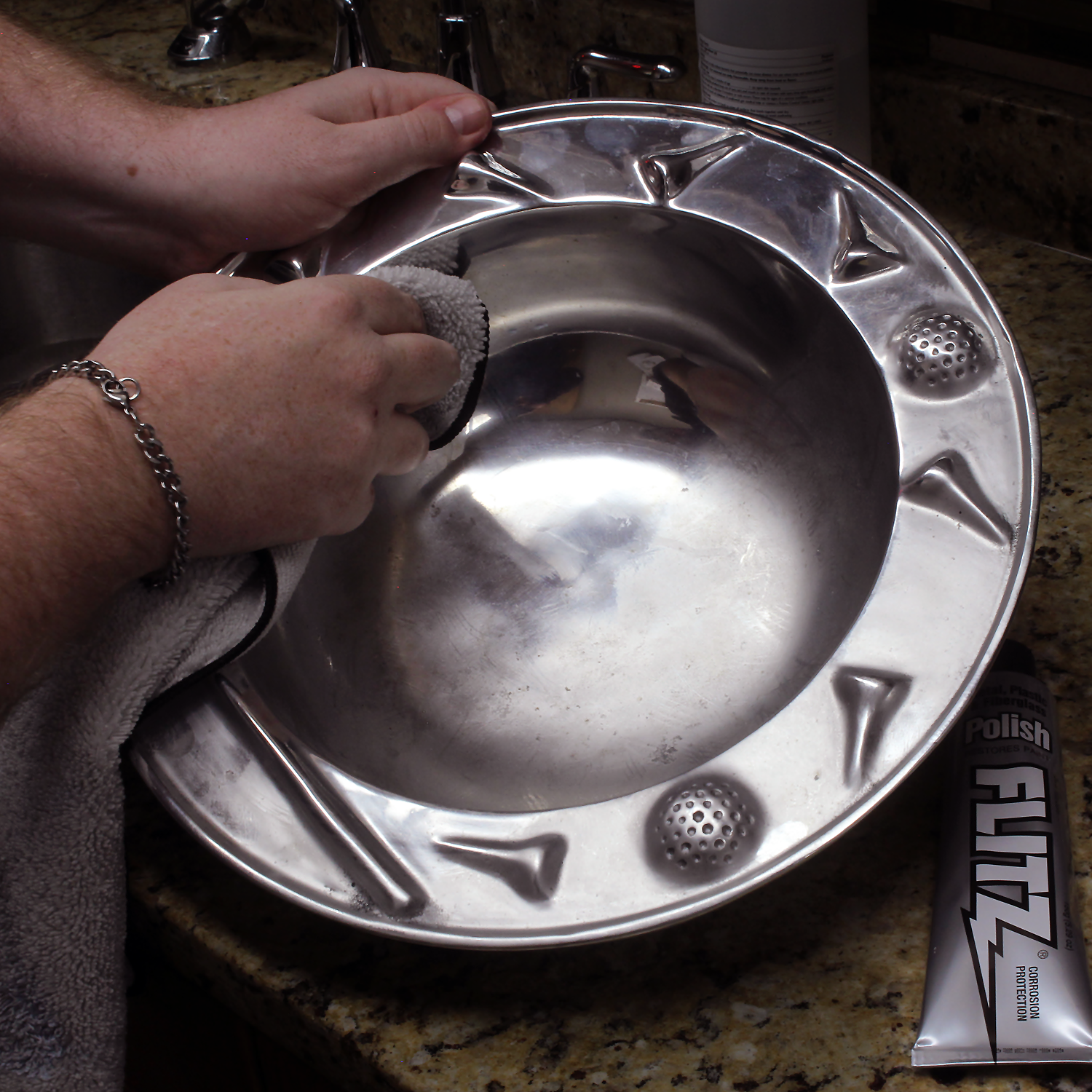 A person uses a rag and metal polish to polish a silver bowl.